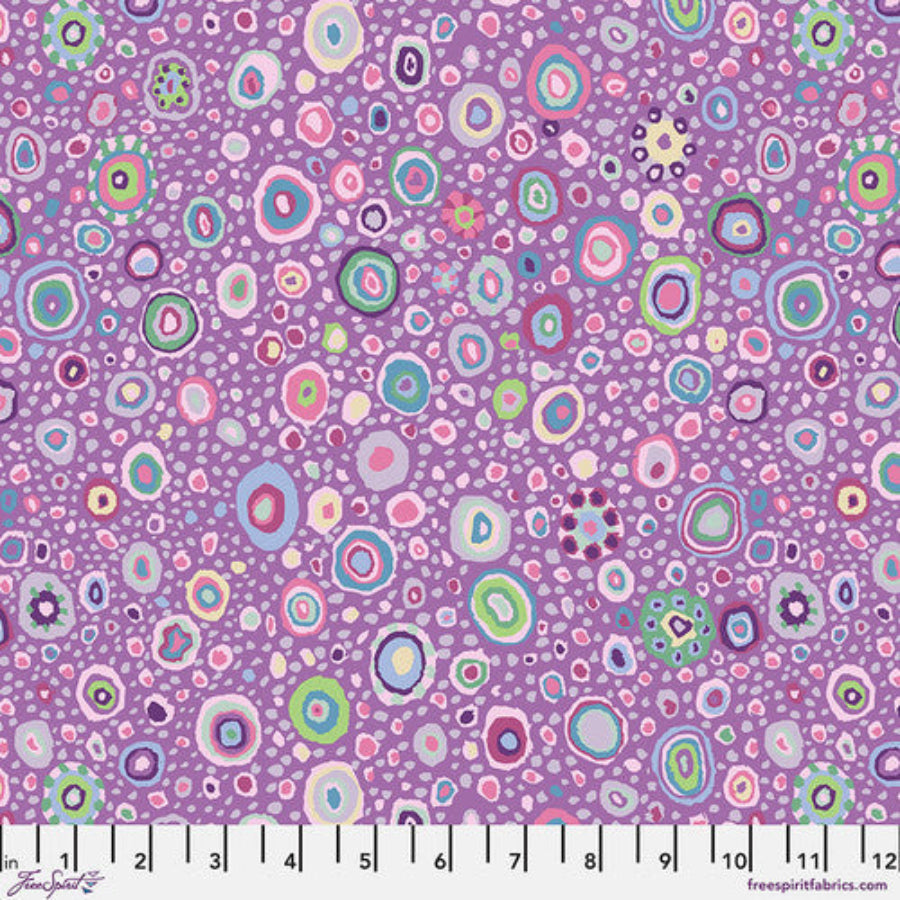 Lähikuva Kaffe Fassett Collectiven Roman Grass Lavender PWGP001.LAVEN -puuvillakankaasta, jossa on täpläkuviointi lilan ja muiden sävyjen vivahteilla. Sopii täydellisesti tilkkutöihin ja ompeluun.