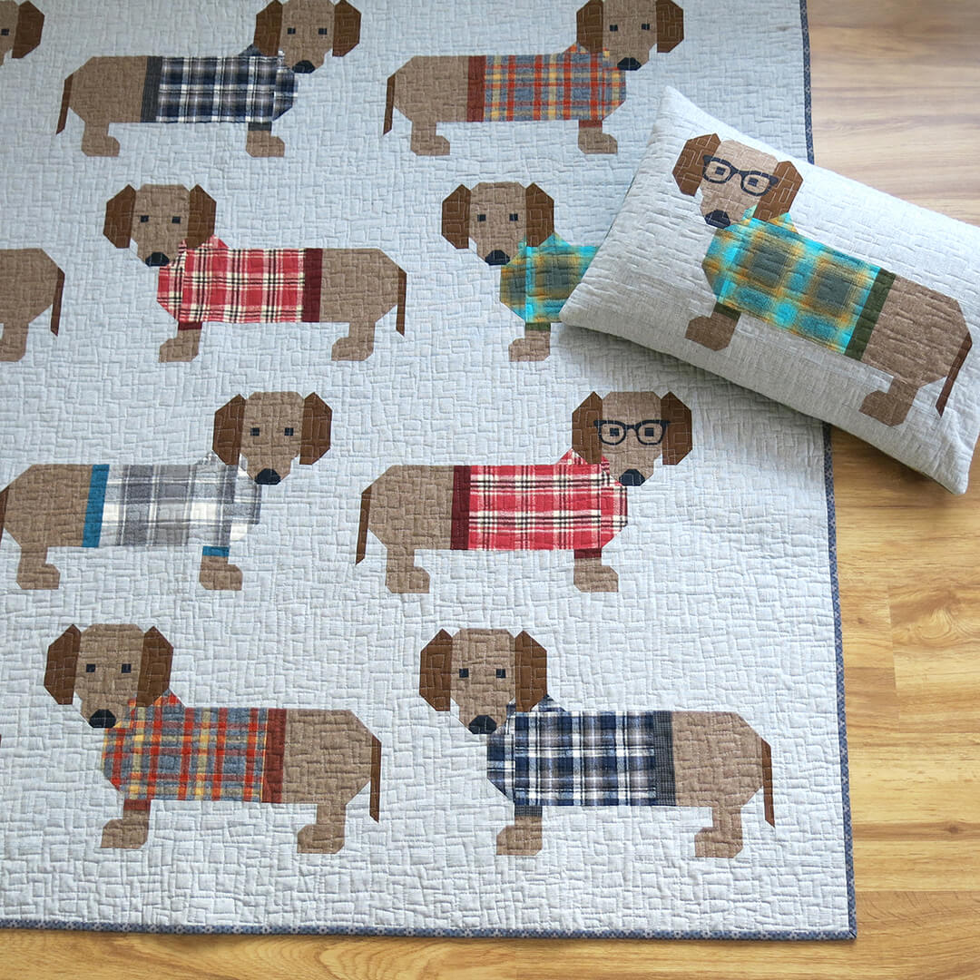Tilkkutyöpeitto, jossa 16 mäyräkoiraa värikkäissä ruutupuseroissa. Malli: Dog in Sweaters – suunnittelija Elizabeth Hartman. Valmis koko n. 185 × 193 cm.