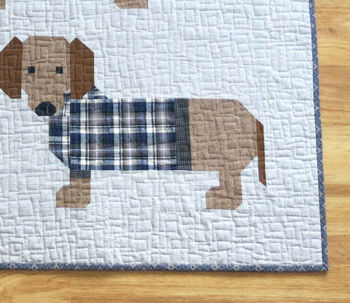 Tilkkutyöpeitto, jossa 16 mäyräkoiraa värikkäissä ruutupuseroissa. Malli: Dog in Sweaters – suunnittelija Elizabeth Hartman. Valmis koko n. 185 × 193 cm.