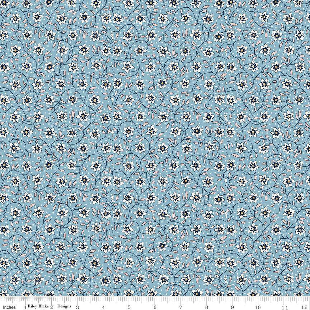 Vaaleansininen puuvillakangas, jossa on Liberty Londonin Denim Florals -kokoelman Lily Trail -kuosi. Kangas on koristeltu pienillä valkoisilla kukilla ja vaaleanpunaisilla lehtikuvioilla.