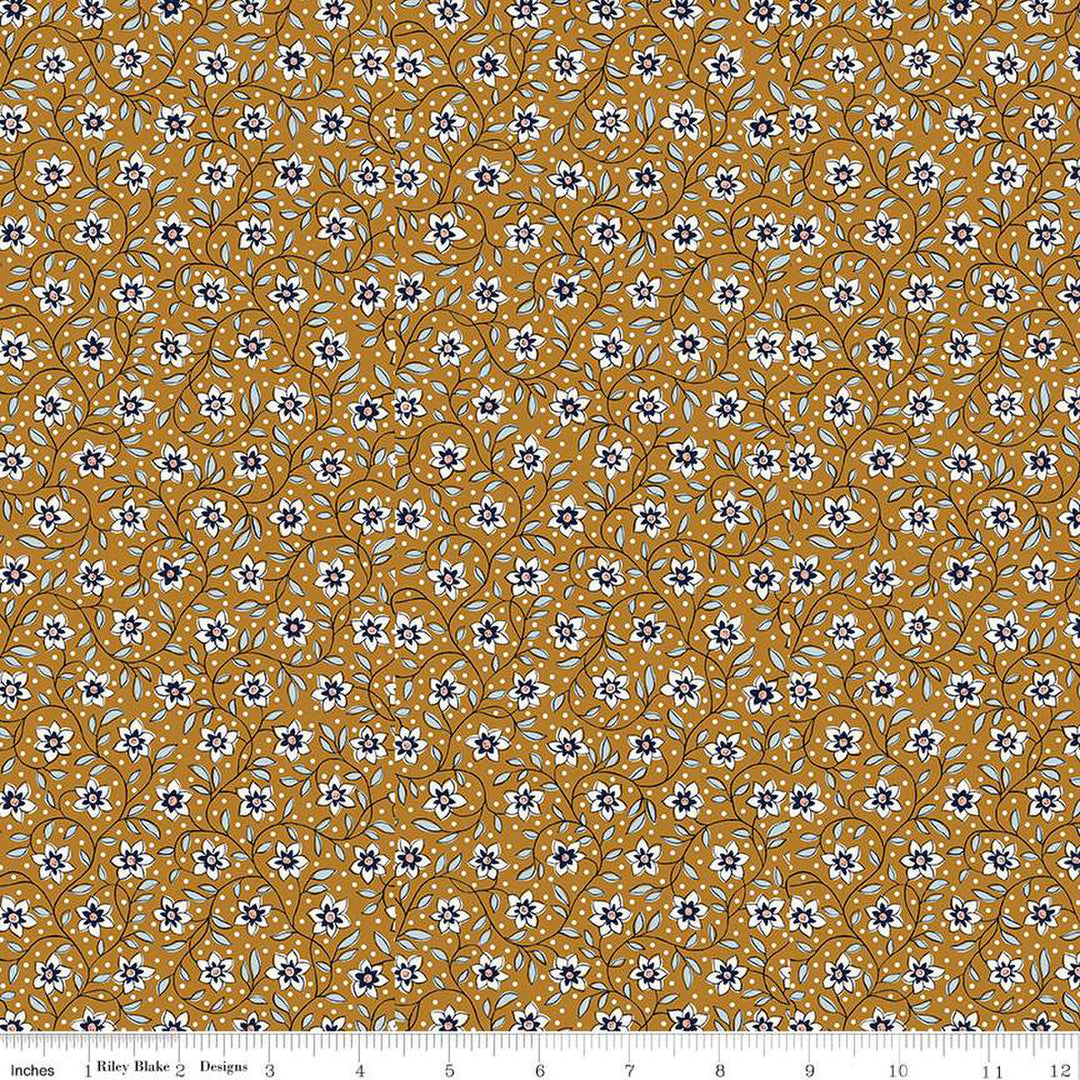 Keltaruskea puuvillakangas, jossa on Liberty Londonin Denim Florals -kokoelman Lily Trail -kuosi. Kangas on koristeltu pienillä valkoisilla kukilla ja sinisillä lehtikuvioilla.