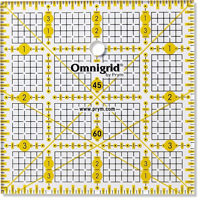 Prym Omnigrid 4×4 tuuman tilkkutyöviivain, kelta-mustat tuumamerkinnät ja kulmaviivat näkyvät läpinäkyvällä viivaimella.