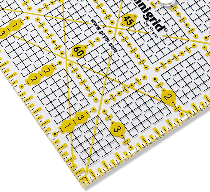 Prym Omnigrid 4×4 tuuman tilkkutyöviivain, kelta-mustat tuumamerkinnät ja kulmaviivat näkyvät läpinäkyvällä viivaimella.