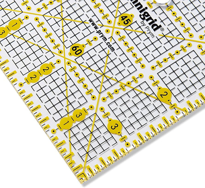 Prym Omnigrid 4×4 tuuman tilkkutyöviivain, kelta-mustat tuumamerkinnät ja kulmaviivat näkyvät läpinäkyvällä viivaimella.