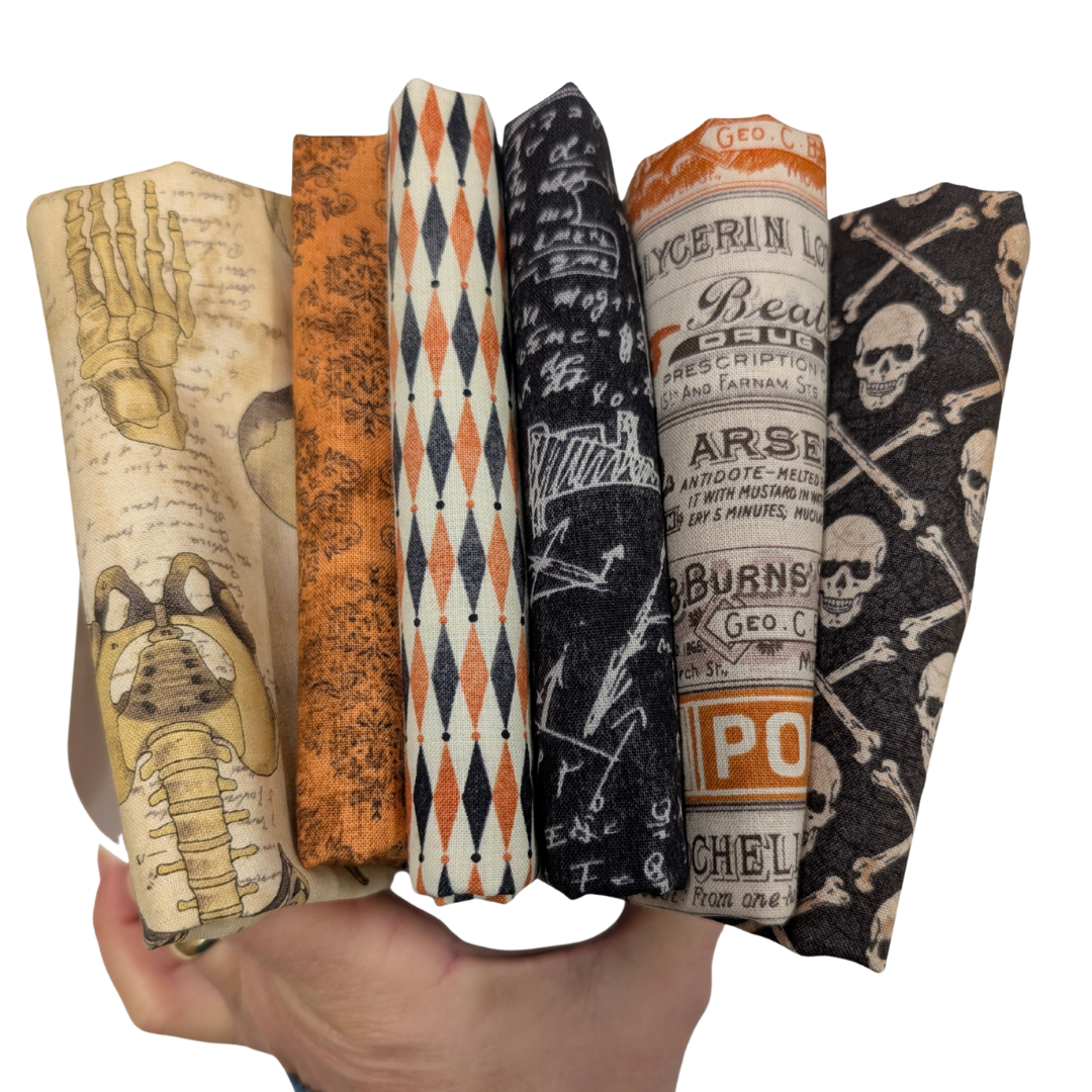 Tim Holtz Halloween Fat Quarter -kangasnippu, 6 vintage-henkistä kangasta, joissa kalloja, geometrisia kuvioita ja vanhoja etikettejä oranssin, mustan ja luonnonvalkoisen sävyissä.