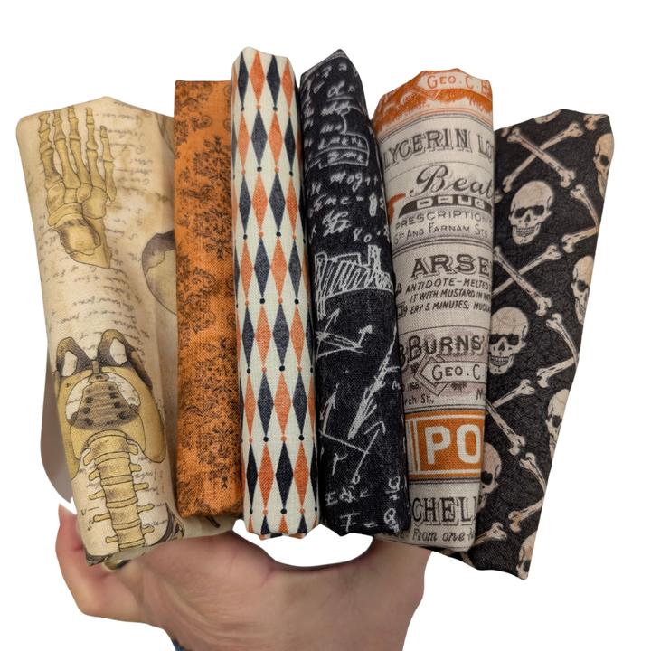 Tim Holtz Halloween Fat Quarter -kangasnippu, 6 vintage-henkistä kangasta, joissa kalloja, geometrisia kuvioita ja vanhoja etikettejä oranssin, mustan ja luonnonvalkoisen sävyissä.