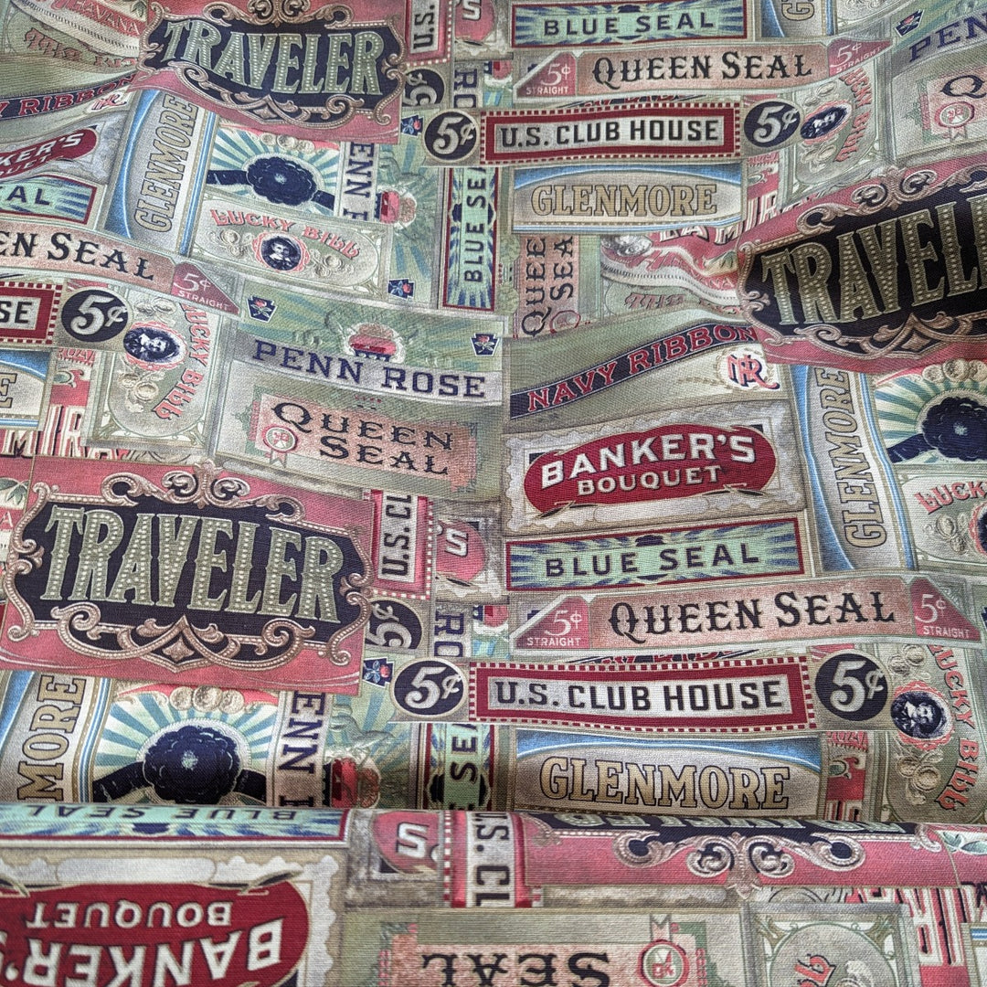 Tim Holtz Embark Cigarbox Canvas -puuvillapanamakangas, jossa vintage-tyylisiä sikarilaatikoiden etikettejä punaisen, vihreän ja beigen sävyissä.